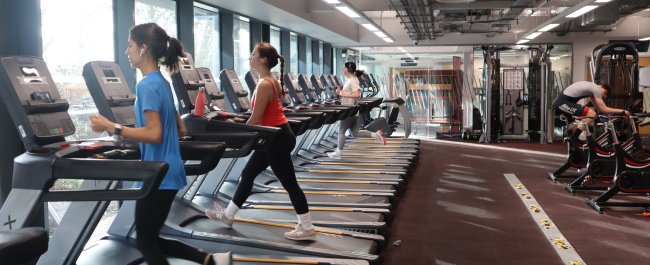 Three females using the treadmills in a gym opposite a male cycling on a static bike.